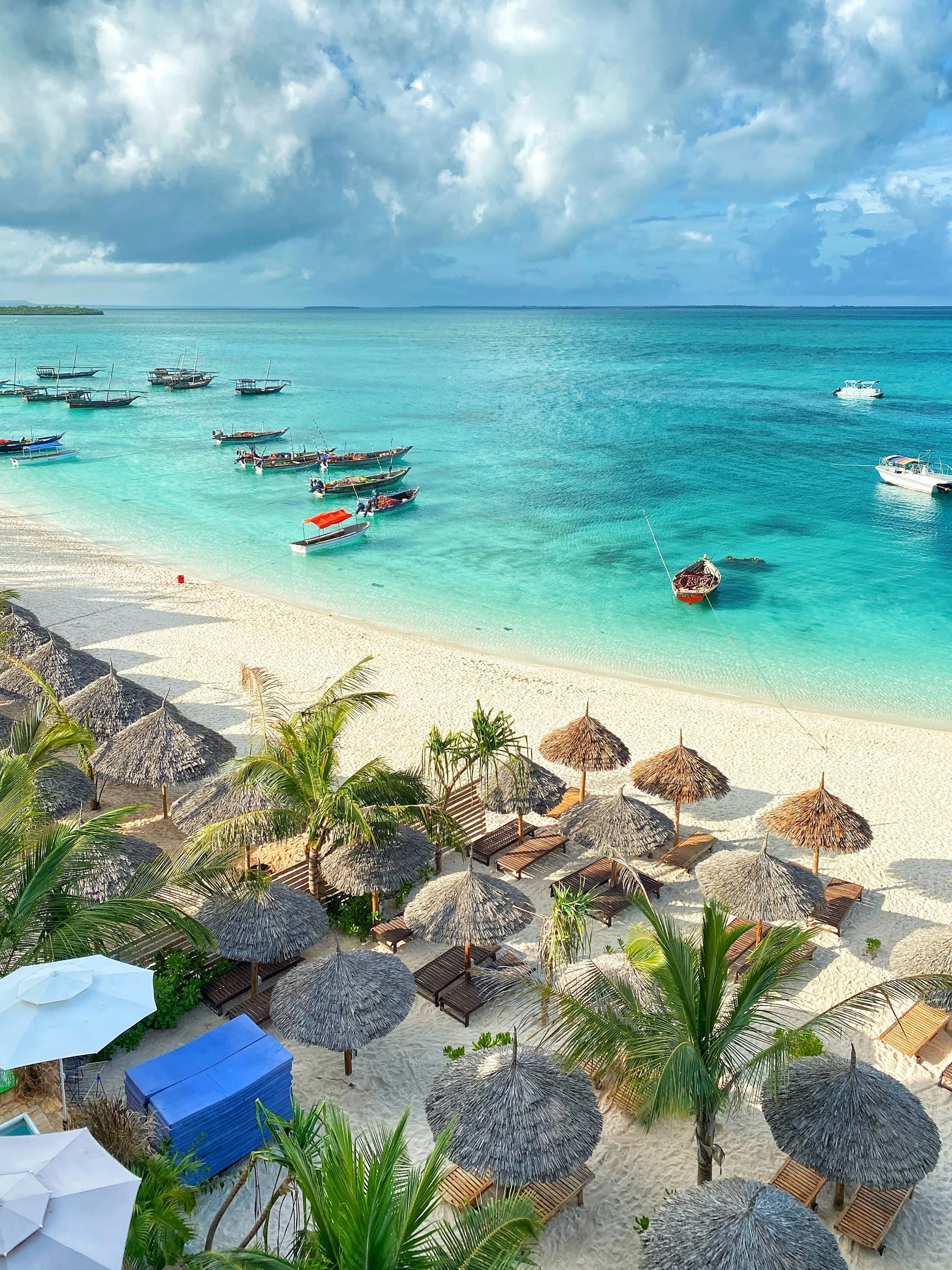 Wooden boats on turquoise water beside a white sand beach in Zanzibar