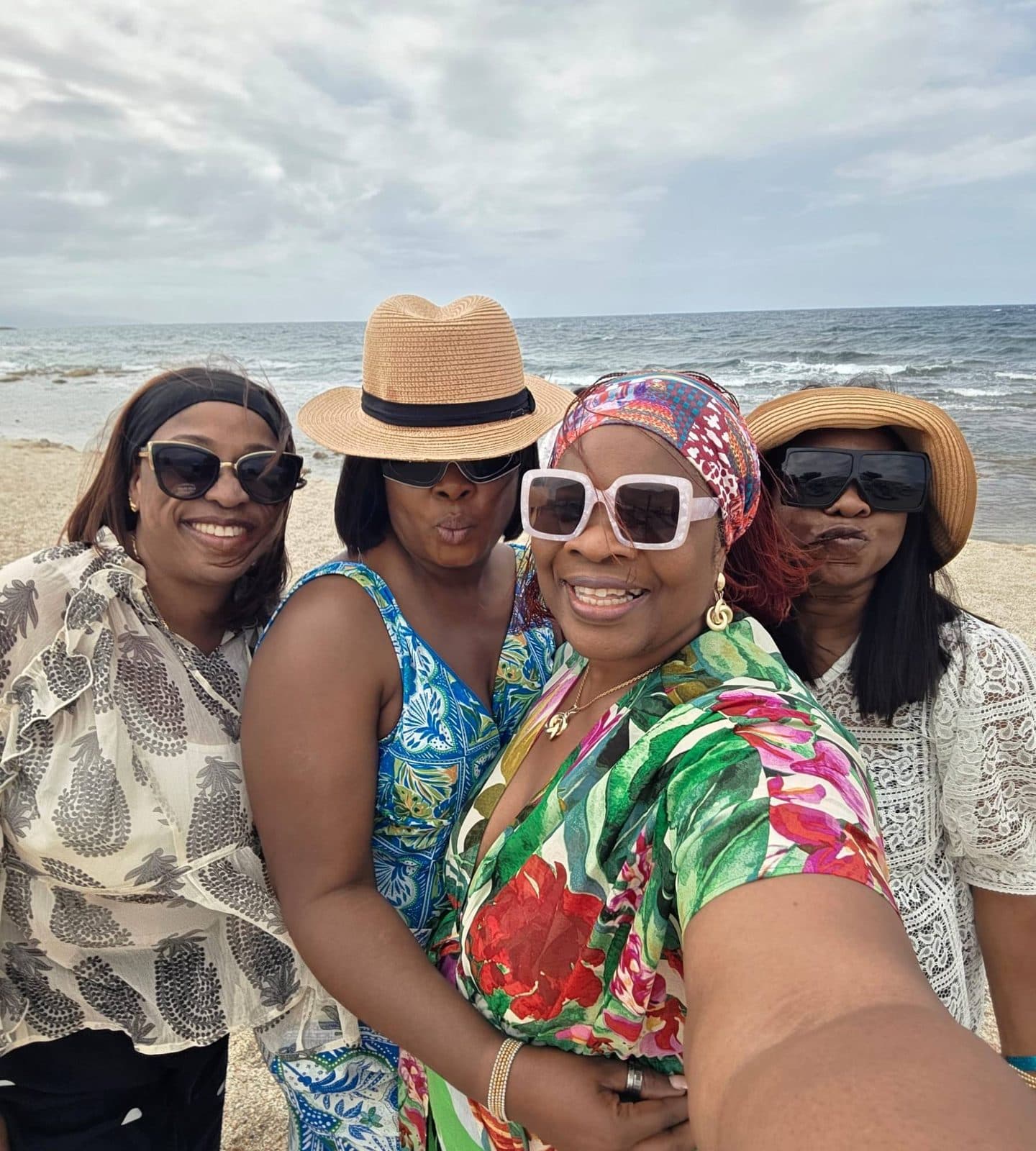 Four women in sun hats and sunglasses taking a selfie on the beach