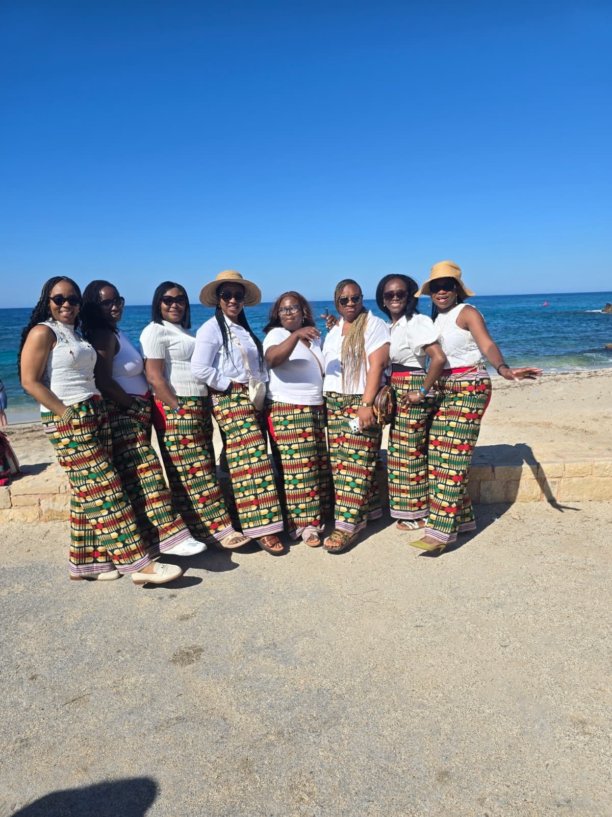 Eight women in white tops and matching printed trousers on a sunny beach