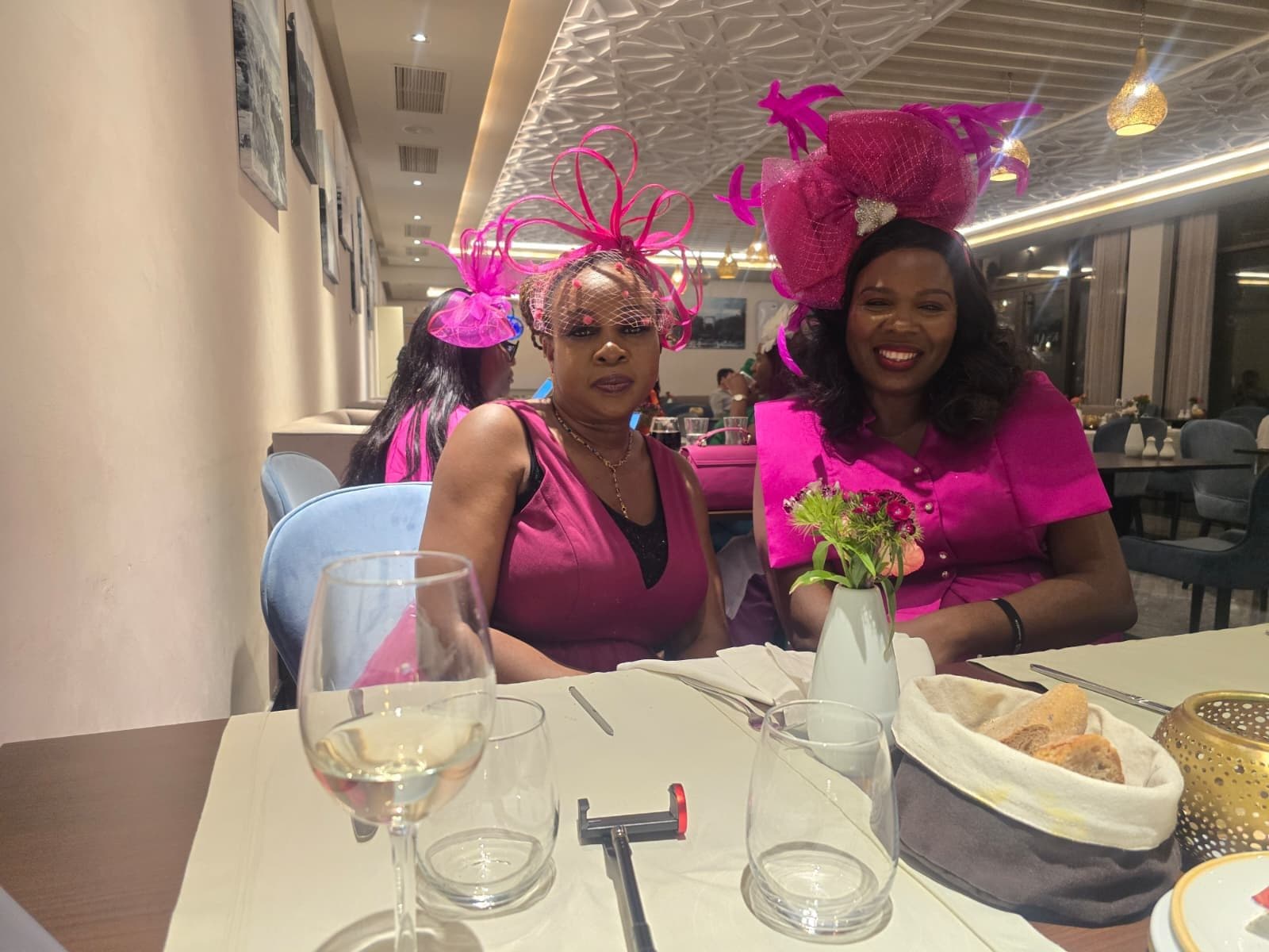 Dinma and Bokun in pink fascinators at a dinner table