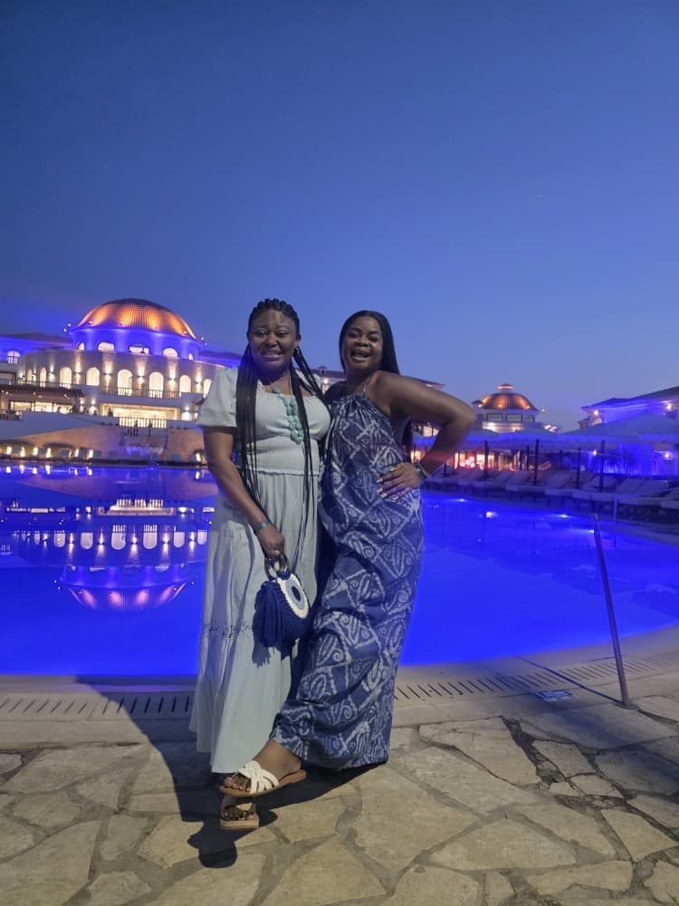 Two women in blue dresses beside a lit pool at night