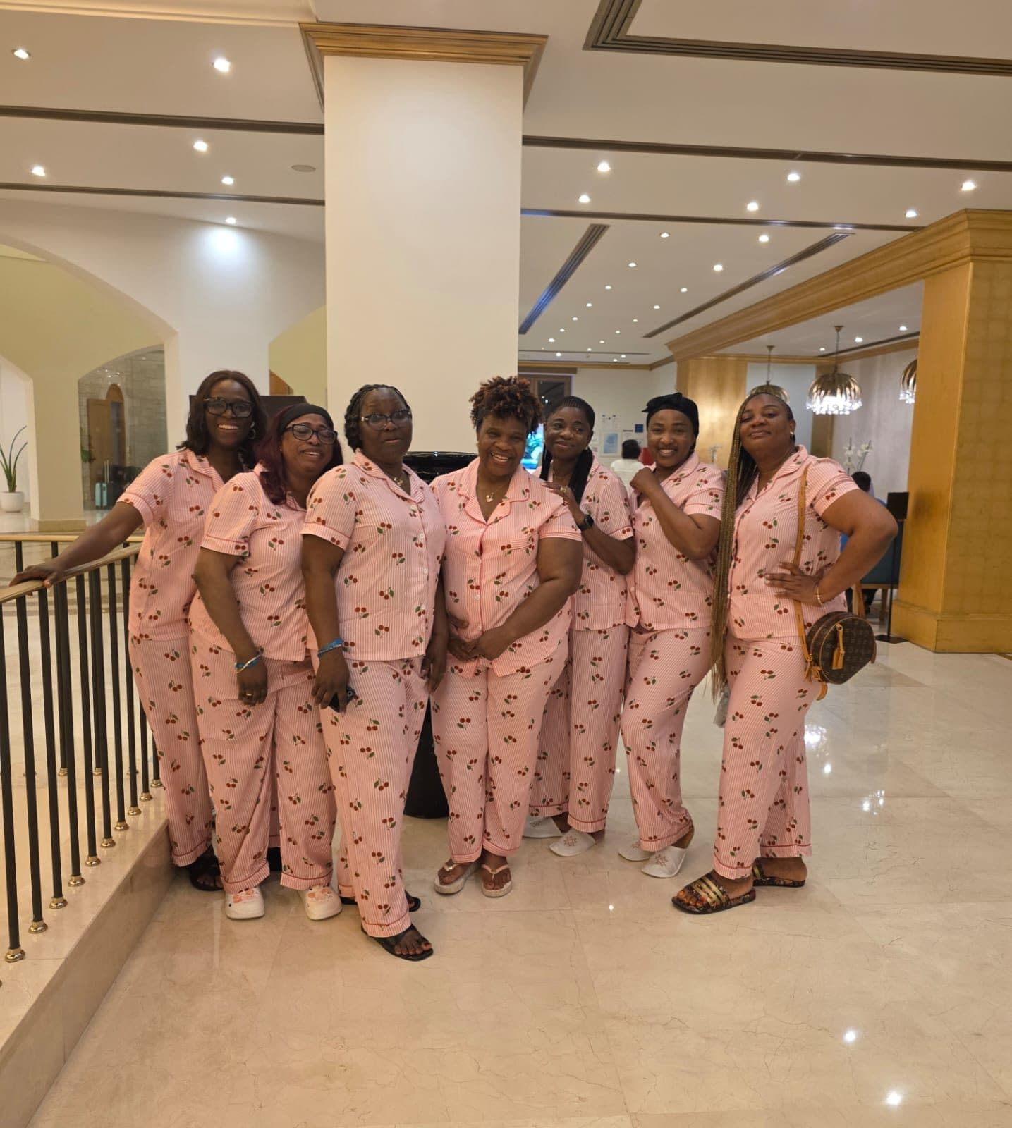 Seven women in matching pink pyjamas laughing in a hotel lobby