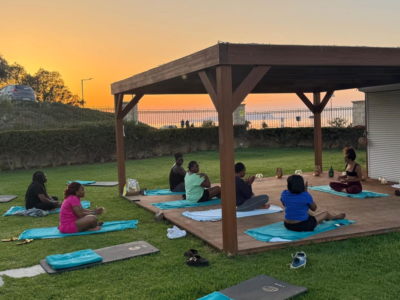 Women sitting on mats under a wooden pergola at sunset