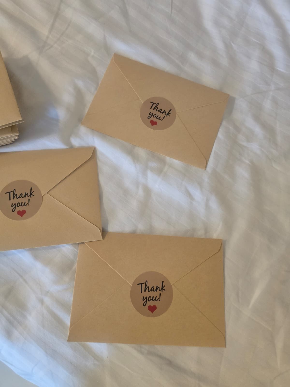 Kraft envelopes with thank-you stickers laid on a bed