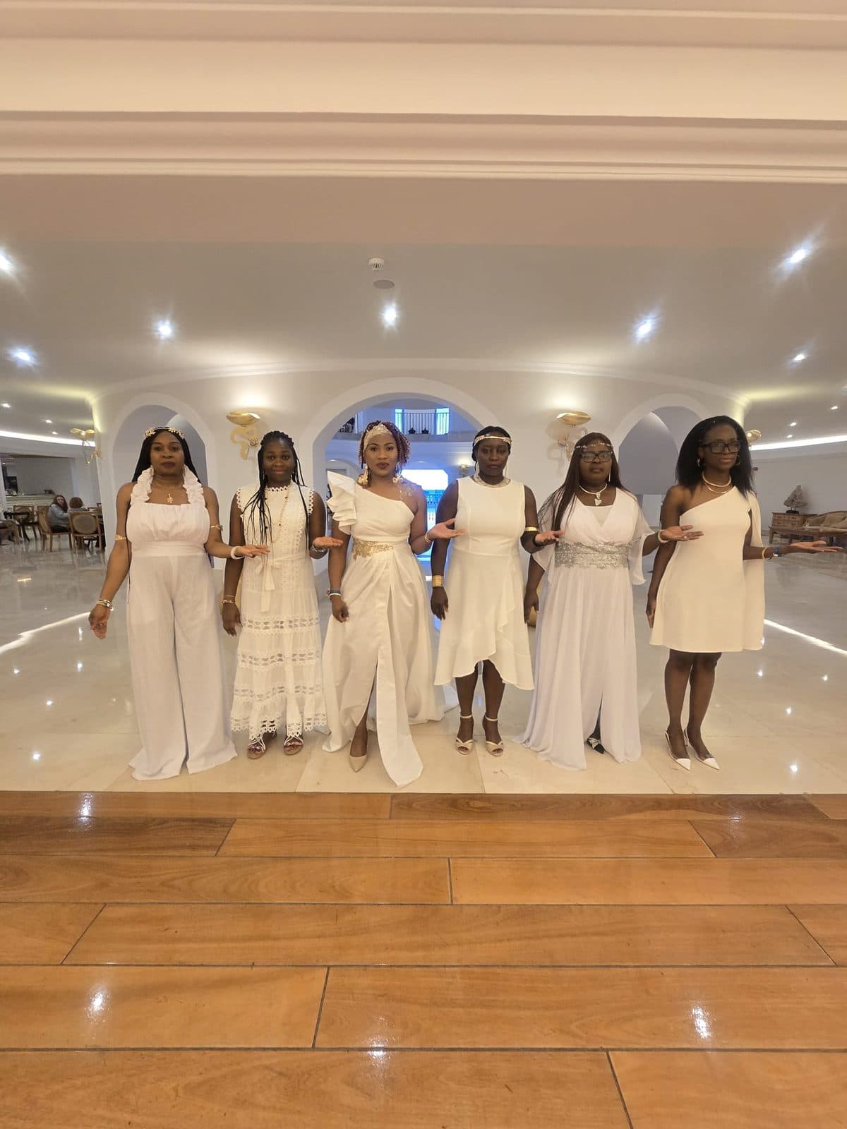 Six women in white dresses posing in a hotel lobby