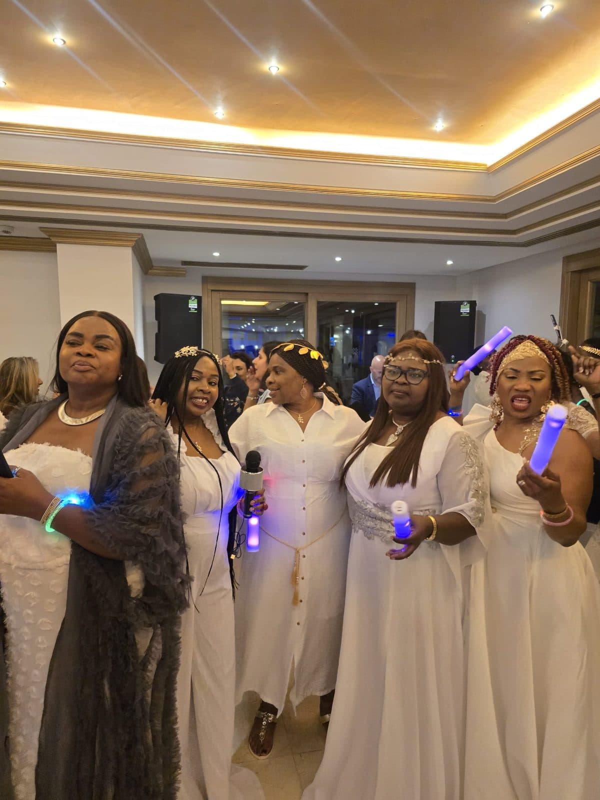 Women in white holding glow sticks and a microphone at a party